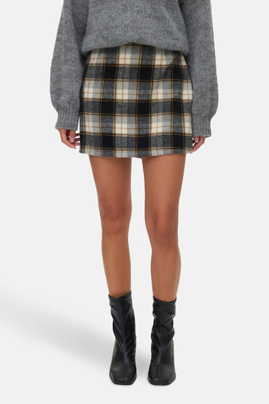 Jupe courte multicolore de VERO MODA, avec motif à carreaux, associée à un pull gris et des bottes noires.