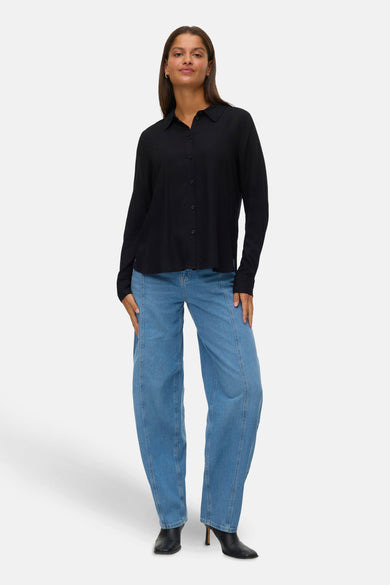 Chemise noire à manches longues de VERO MODA, portée avec des jeans bleus à taille haute et des bottes noires.