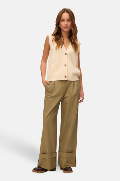 Gilet beige de Vero Moda, avec fermeture à boutons et poches brodées, porté avec un pantalon kaki et des chaussures brunes.