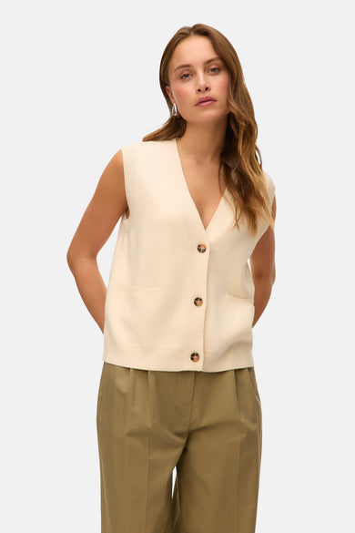 Gilet beige de VERO MODA, avec fermeture à boutons, poches et porté sur un pantalon vert olive.