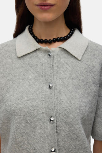 Gilet gris de VERO MODA avec des boutons argentés et un col, porté avec une chaîne de perles noires.