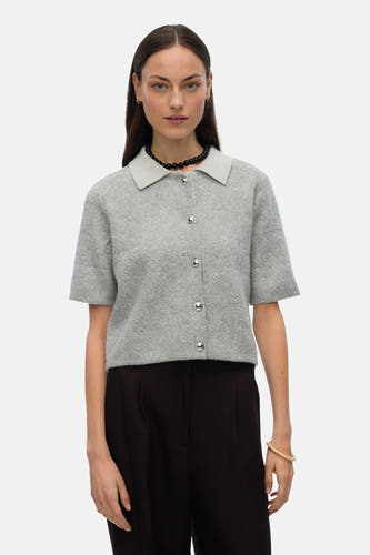 Gilet gris de VERO MODA, avec des manches courtes, des boutons argentés et porté avec une chaîne de perles noires.