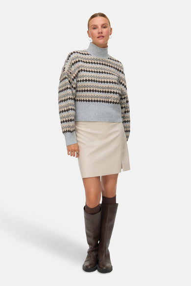 Sweat-shirt multicolore à col montant de VERO MODA, avec un motif à carreaux géométriques, associé à une jupe crème et des bottes brunes.