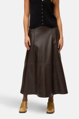Long manteau brun de VERO MODA, avec des broderies décoratives, associé à une chemise noire et des mocassins bruns.