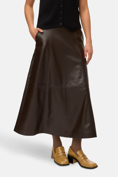 Jupe longue brune de VERO MODA, avec des coutures verticales et portée avec un collant brun et des chaussures dorées.