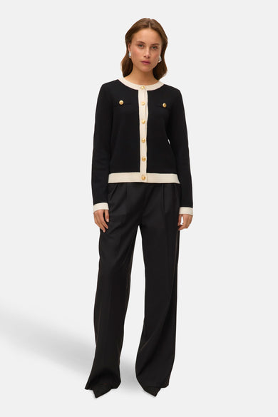 Gilet noir de VERO MODA avec des boutons dorés, associé à un pantalon noir à larges jambes et des boucles d'oreilles argentées.