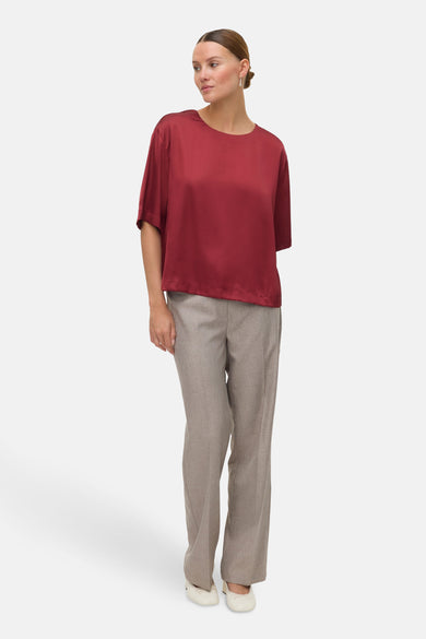 Blouse rouge à manches courtes de VERO MODA®, portée avec un pantalon gris et des ballerinas crème.
