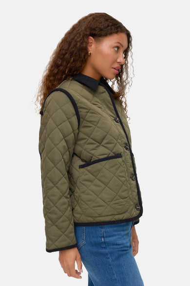 Manteau court vert de Vero Moda, avec des strass et une finition noire, porté avec un jean bleu.