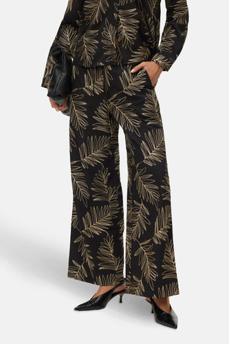 Vrouw in zwart met gouden bladmotief pak en zwarte leren handtas en schoenen.