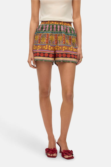 Short multicolore de VERO MODA®, avec un motif de plantes tropiques et de coquillages, associé à une chemise blanche et des chaussons rouges.