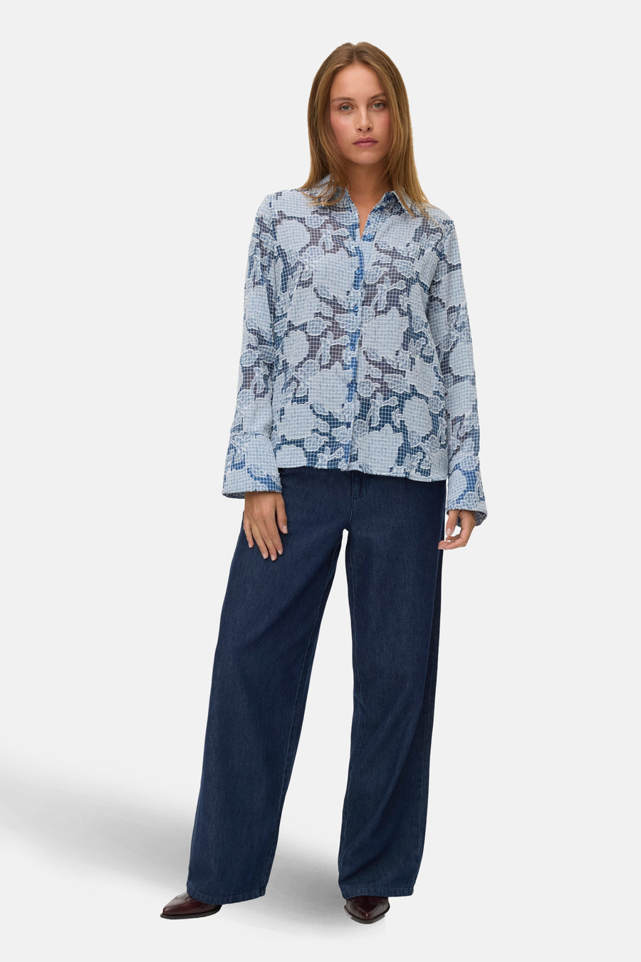 Vrouw draagt blauwe blouse met bloemenprint en donkerblauwe jeans.