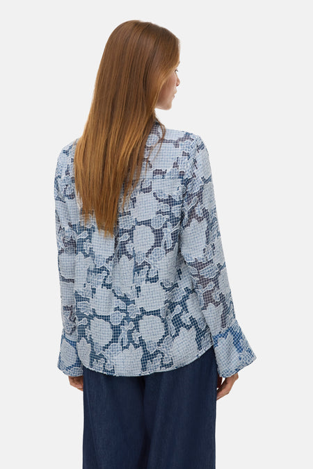 Vrouw in blauwe blouse met bloemenpatroon, van achteren gezien.