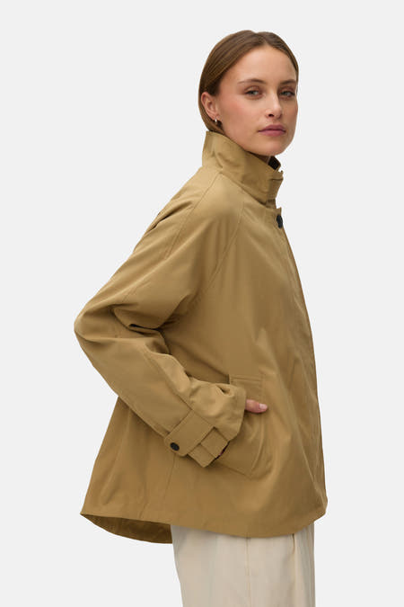 Manteau court beige de VERO MODA, avec col montant et manches longues, combiné avec un pantalon de couleur crème et des talons noirs.