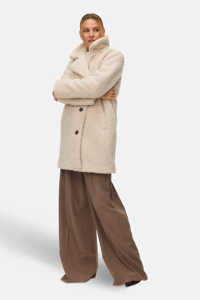 Manteau long beige de VERO MODA, avec des manches croisées porté sur une jupe brune et large.