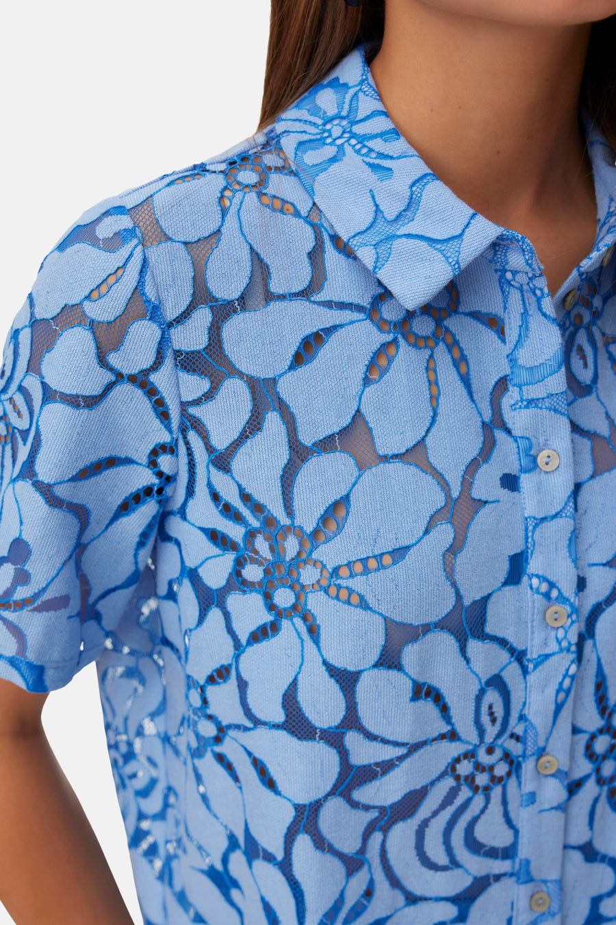 Chemise bleue à manches courtes de VERO MODA, avec un motif de dentelle florale détaillé et des boutons visibles.