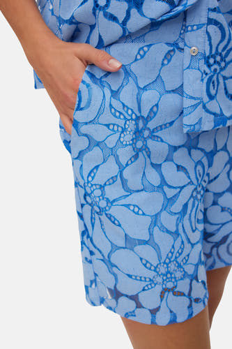Short bleu VERO MODA® avec motif de dentelle florale, une main dans la poche et un bouton.