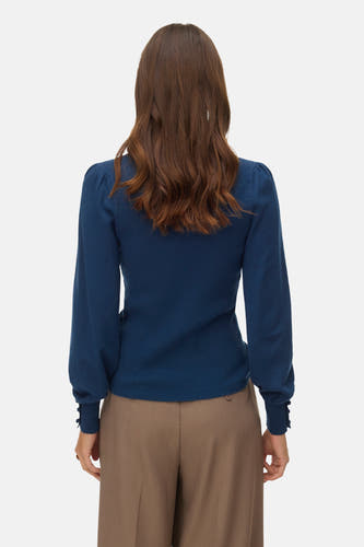 Blauwe trui met ronde hals van VERO MODA®, rugaanzicht, lange mouwen met knoopjes, gecombineerd met een bruine pantalon.
