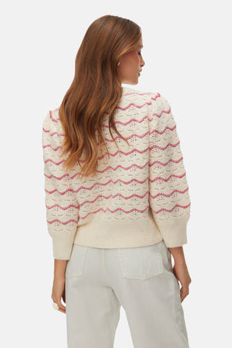 Gebreide trui met ronde hals van VERO MODA, met rood zigzagpatroon en driekwart mouwen, gedragen met een witte broek.
