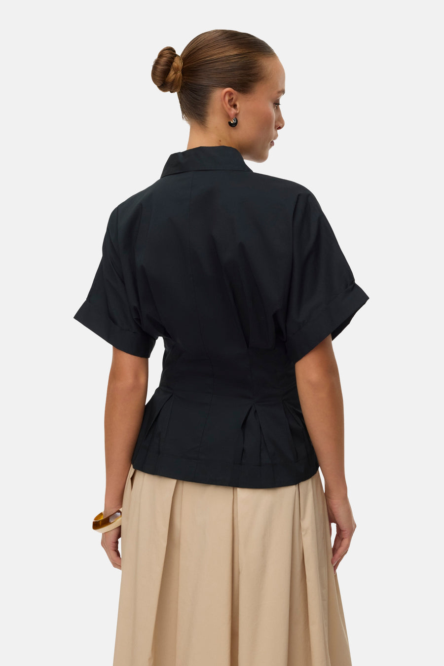Chemisier noir à manches courtes retroussées de VERO MODA® avec taille péplum plissée, dos sur mannequin avec jupe plissée beige.
