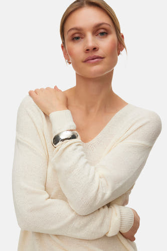 Pull col V écru de VERO MODA®, porté avec un pantalon large marron et des talons marron.