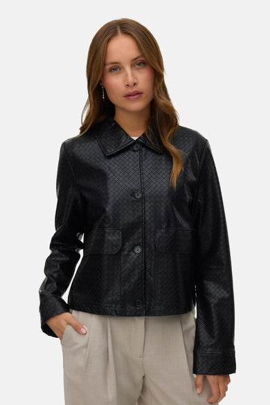 Manteau court noir de VERO MODA, avec une texture tissée et une fermeture à boutons, associé à un pantalon beige.