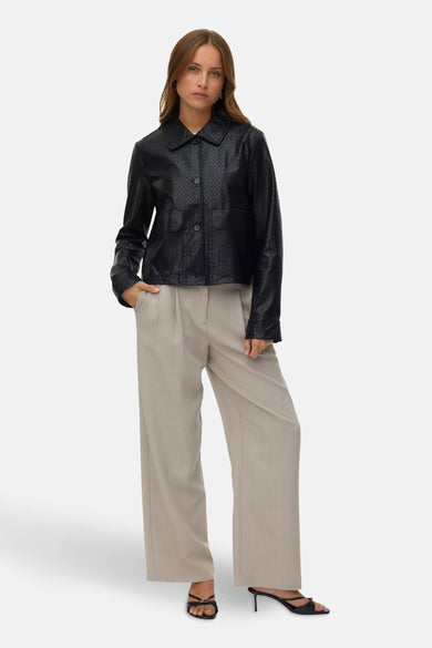Manteau court noir de VERO MODA, avec un motif de carreaux tissé, associé à un pantalon beige et des chaussures ouvertes noires à talons.