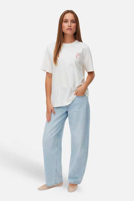 Wit T-shirt van VERO MODA met rood kreeftenmotief op de borst, gedragen met lichte jeans en nude ballerina's.