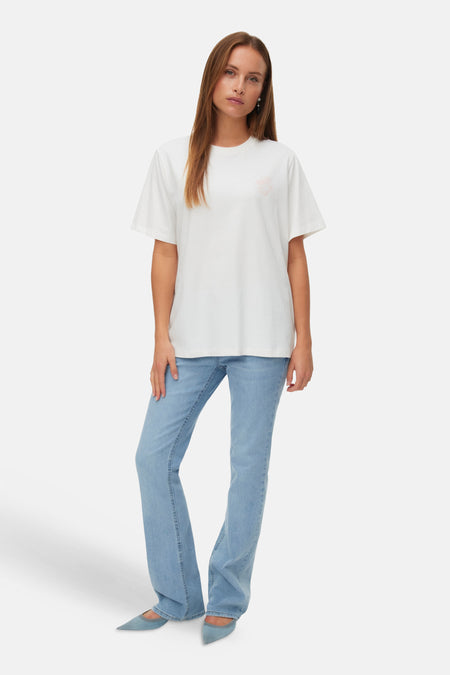 Wit T-shirt van VERO MODA met lichtroze borstprint, gedragen met een lichtblauwe jeans en puntige lichtblauwe ballerina's.