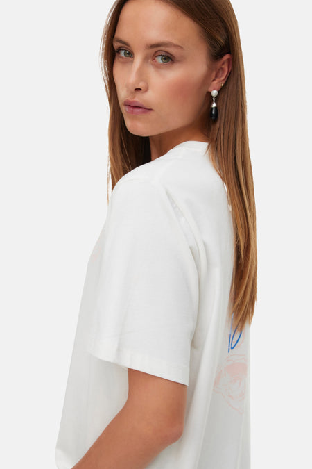 T-shirt blanc à manches courtes de VERO MODA avec imprimé abstrait rose et bleu dans le dos, porté par un mannequin de profil.