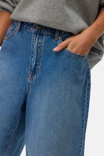 Short en jean bleu de VERO MODA, avec poche latérale, porté avec un pull gris.