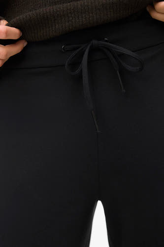 Pantalon noir de VERO MODA avec une ceinture élastique à la taille, porté avec un pull marron.