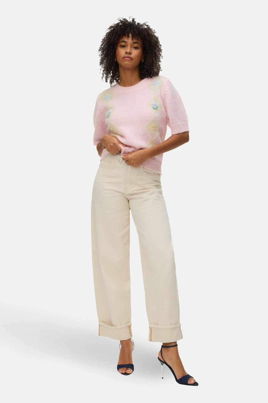 Roze trui met ronde hals van VERO MODA®, versierd met bloemendetails en gecombineerd met crèmekleurige jeans en donkerblauwe hakken.
