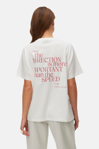 T-shirt blanc à manches courtes de VERO MODA, avec impression de texte rouge, associé à un jean léger et des chaussures noires.
