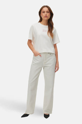 Wit T-shirt met korte mouwen van VERO MODA, met rode tekstprint, gecombineerd met een lichte jeans en zwarte schoenen.