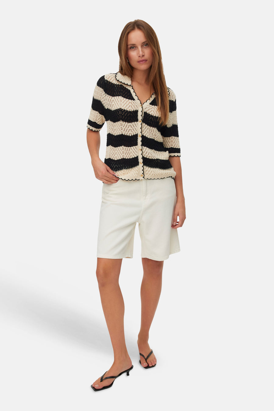 Gilet met zwarte en gebroken witte strepen van VERO MODA®, gehaakt met geschulpte randen en knopen, gedragen met crèmekleurige shorts en slippers.