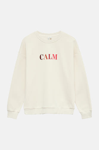 Pull écru à col rond de Vero Moda, avec le texte "CALM" dans des tons marron et rose.