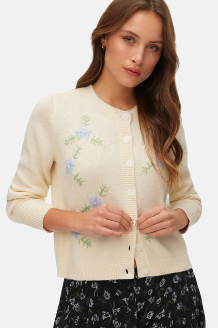Ecru gilet van VERO MODA, met blauwe bloemen en groene bladeren, dichtgeknoopt over een rok met bloemenprint.