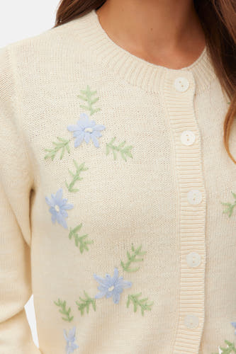 Gilet écru de VERO MODA, orné de délicates fleurs bleu clair et de brindilles vertes brodées.