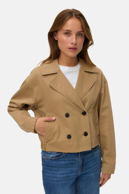 Bruine jas van Vero Moda met dubbele knoopsluiting, steekzak en blauwe jeans.
