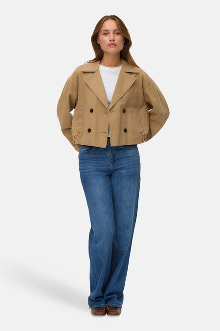 Bruine korte jas van Vero Moda met dubbele knoopsluiting, gedragen met een wit T-shirt en wijde jeans.