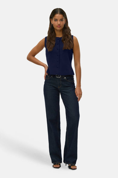 Gilet bleu de Vero Moda, avec fermeture à boutons, associé à un pantalon de cuir foncé et des baskets noires.