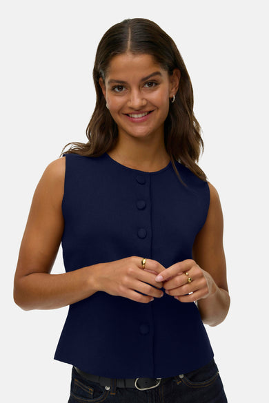 Gilet bleu de VERO MODA, avec fermeture à boutons, porté avec un jean et une ceinture.