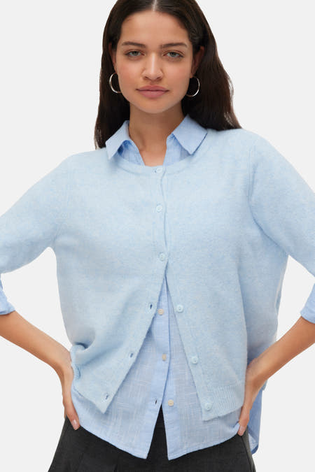 Veste bleue de VERO MODA, portée sur des manches longues sur une chemise bleu clair et une jupe grise foncée.