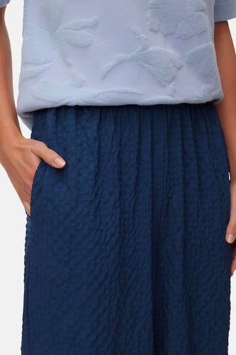 Pantalon bleu de VERO MODA avec taille plissée et texture froissée, main dans la poche.