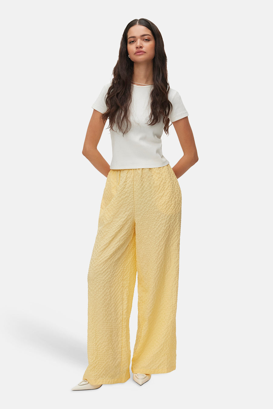 Gele broek van VERO MODA® met een textuurmotief, gecombineerd met een wit shirt en parelketting.