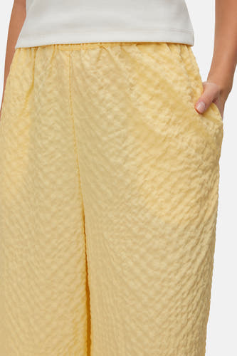 Pantalon jaune de VERO MODA, avec taille élastique et tissu texturé, et une main dans la poche.