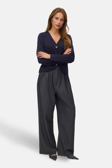 Gilet bleu de VERO MODA®, avec des manches longues, une fermeture à boutons et porté avec un pantalon gris large et des escarpins pointus.