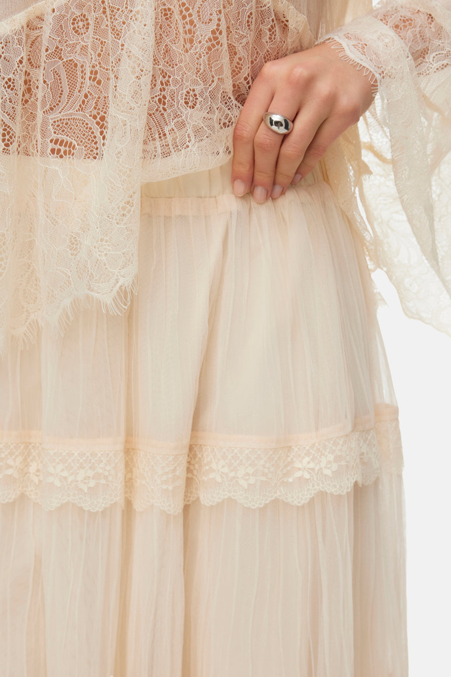 Longue jupe écru de VERO MODA, avec des détails sur les bords des couches et une bague d'argent à la main.