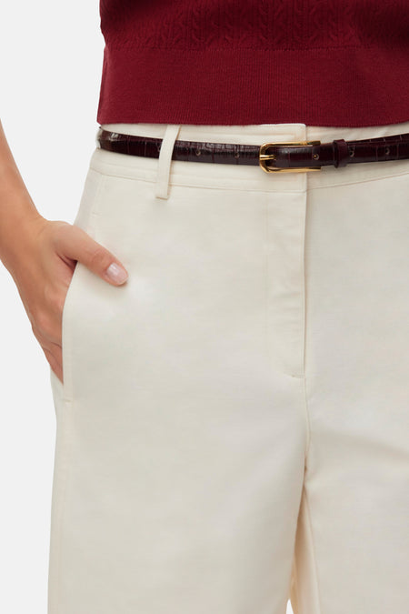Bermuda écru de VERO MODA, portée à la taille avec une fine ceinture marron foncé à imprimé crocodile et une main dans la poche.