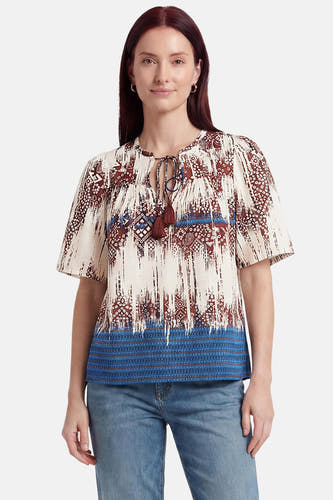 Multicolor blouse met korte mouwen van VERO MODA, met abstracte print in bruin, wit en blauw, split-halslijn met kwastjes en gebreide blauwe zoom, gedragen met jeans.